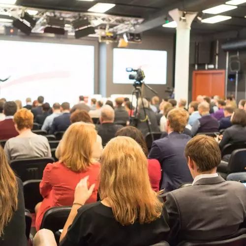 Banner image with a photograph of a crowded audience watching a presentation in a conference hall.