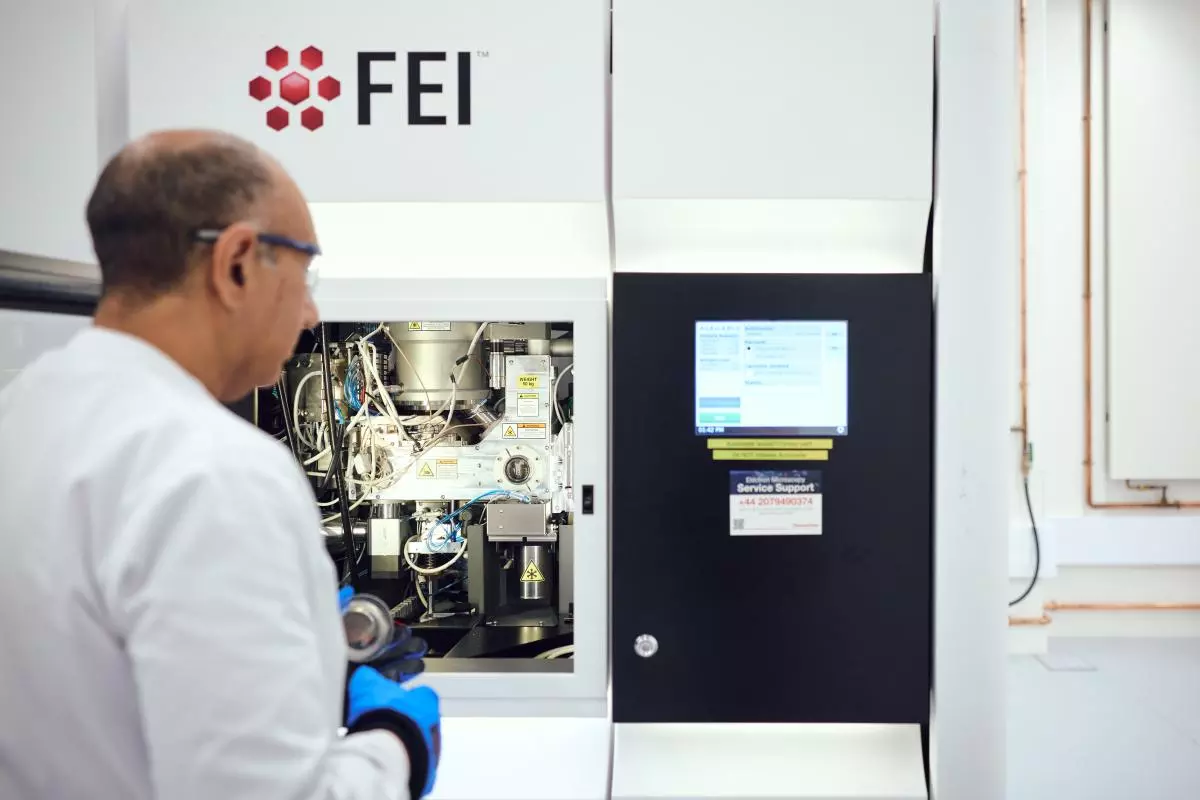 A scientist wearing blue gloves operates a large cryo-EM in a laboratory, inspecting its internal components beside a digital control screen.